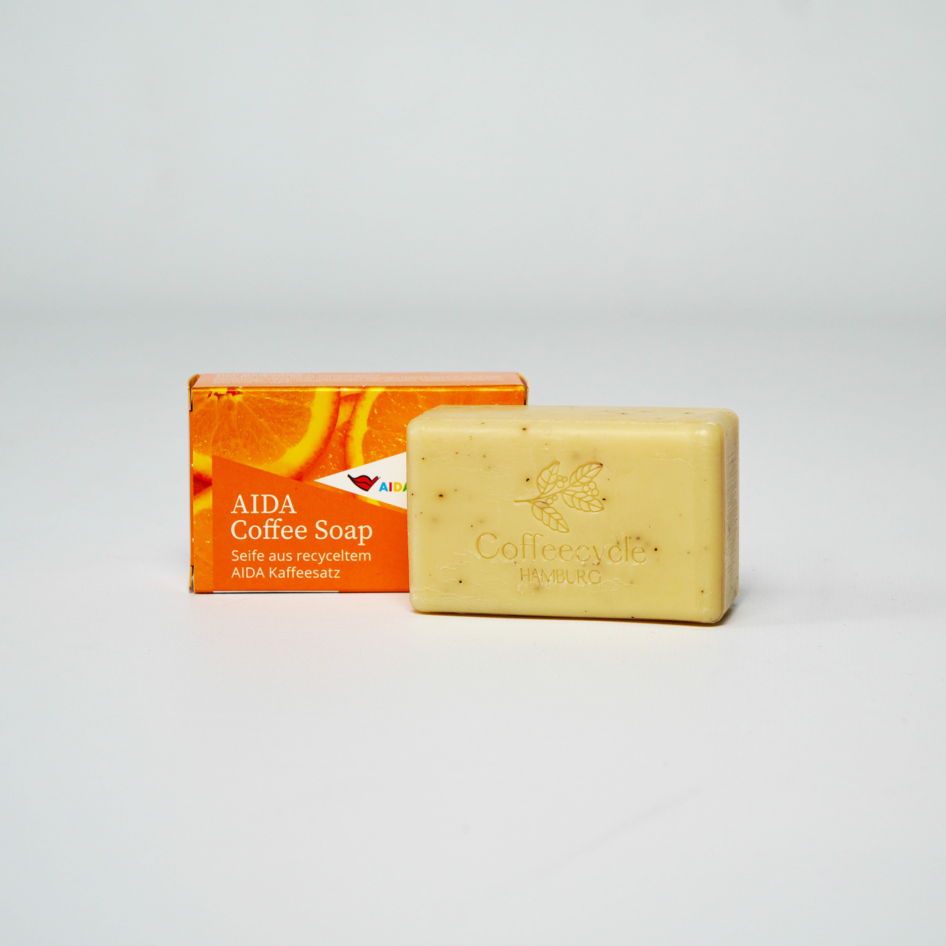 Rechteckiger Seifenblock mit marmorierter Oberfläche in Braun-Orange-Tönen, Verpackung mit orangener Grafik und Schriftzug im Hintergrund – Kaffeeseife Orange.